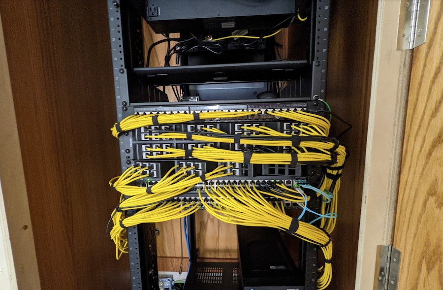 Networking rack installed in a client’s home with several yellow connection cables organized neatly.