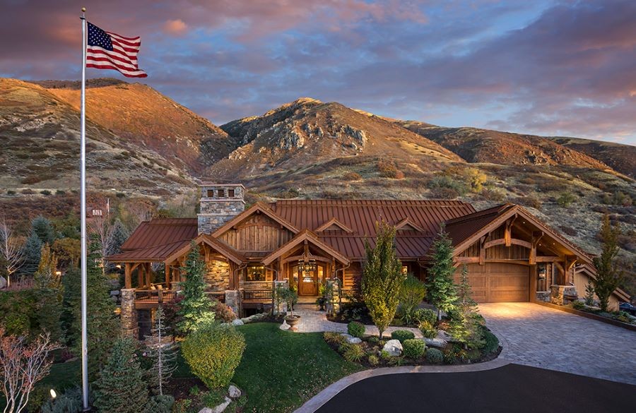 A home with a raised flag and beautiful outdoor lighting surrounded by hills.